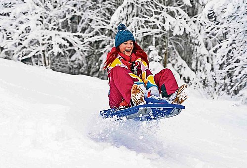 junge Frau in Schneekleidung rodelt mit ihrem Schneebob einen schneebedeckten Berg hinunter