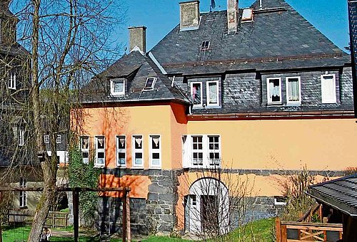 ein großes altes Haus mit Schieferdach im Vordergrund ein Garten mit Spielgeräten