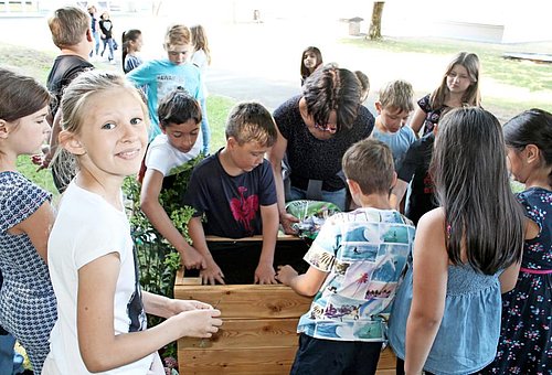 Das Bild zeigt eine Gruppe von Kindern der Grundschule Ludwigsstadt, die gerade ein Hochbeet bepflanzen.