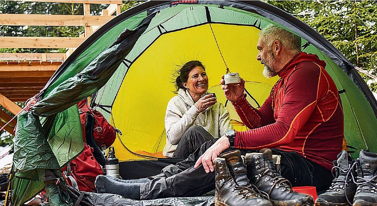 Ein Mann und eine Frau sitzen vor einem kleinen Zelt und trinken aus Tassen.