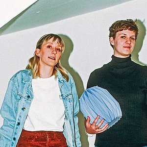 zwei Frauen stehen in einem Treppenhaus, eine hält eine Papierurne in der Hand, eine zweite Urne steht zu Füßen der Frauen