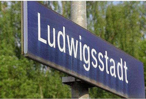 Das Bild zeigt ein Bahn-Haltestellenschild mit dem Namen Ludwigsstadt 