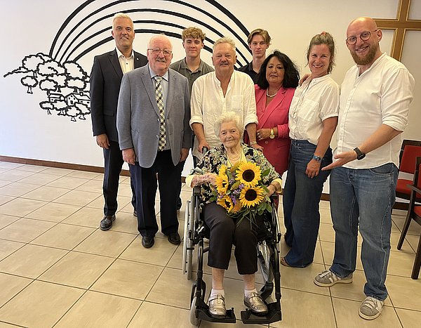 Eine Seniorin sitzt in einem Rollstuhl, hat einen Sonnenblumenstrauß und lächelt in die Kamera. Hinter ihr stehen Männer und Frauen - ihre Familie sowie Bürgermeister Timo Ehrhardt und Landrat-Stellvertreter Bernd Steger.