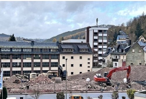 Das Foto zeigt die Baustelle, auf der das Gebäude der Sparkasse abgerissen wird. Zu sehen sind große Bauschuttberge und ein Bagger. 