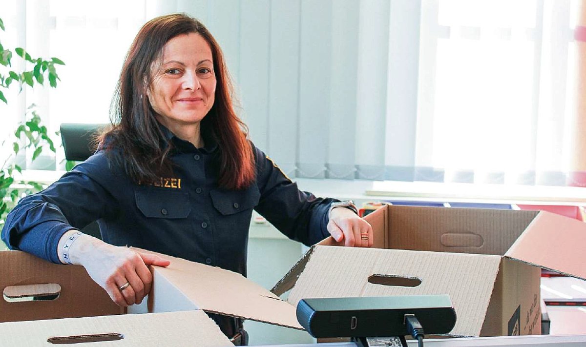 Eine Frau in Polizeiuniform sitzt am Schreibtisch mit zwei offenen Umzugskartons. Sie lächelt in die Kamera.