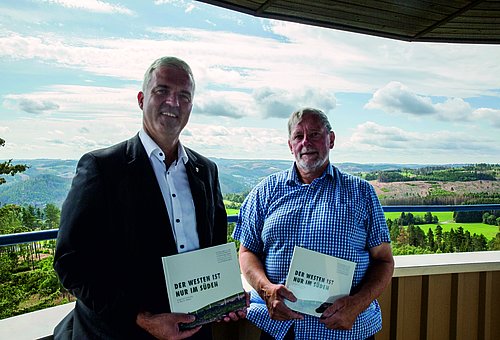 Bürgermeister Timo Ehrhardt und Siegfried Scheidig stehen auf einer Aussichtplattform und halten je ein Buch in der Hand.