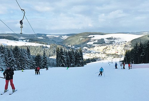 einige Skifahrer auf einem schneebedeckten Hang mit dem Ort im Hintergrund