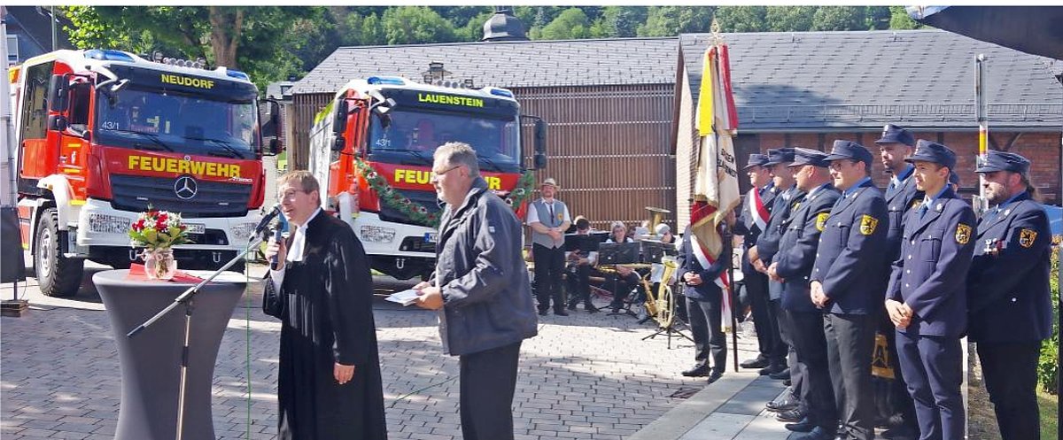 Auf dem Bild sind im Hintergrund zwei neue Feuerwehrfahrzeuge LF 10 zu sehen. Im Vordergrund Pfarrer und Pastoralreferent sowie Feuerwehrkameraden.
