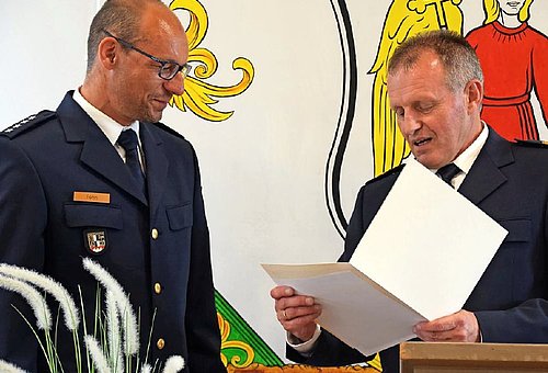 Zwei Polizisten in Uniform. Der eine liest aus einer weißen Mappe etwas vor, der andere ist der neue Leiter der Polizeiinspektion Ludwigsstadt. Er hört gespannt zu. 